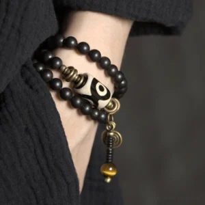 Hand wearing paired Tibetan Dzi bead ebony wood protection bracelets on wrist with double-layer styling