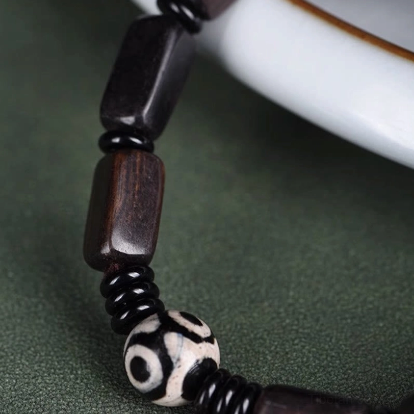 Macro close-up of two-eye Dzi bead and wooden segments showing natural wood grain and bead craftsmanship