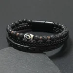 Black leather Nine-Eye Dzi bead lava rock wealth bracelet with magnetic buckle displayed on dark stone, front view