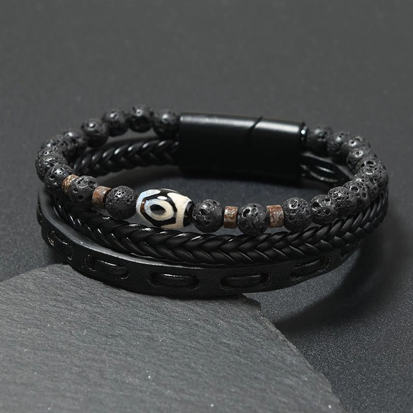 Black leather Nine-Eye Dzi bead lava rock wealth bracelet with magnetic buckle displayed on dark stone, front view