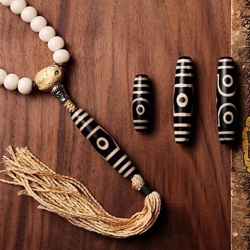 Close-up of dzi bead and mala necklace accessories showing white bodhi seeds and black-white agate dzi bead with cotton tassel on wooden table