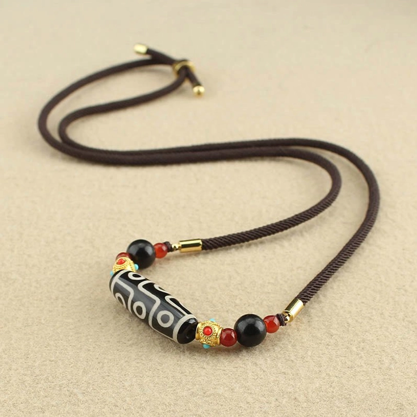 Black-white nine-eye dzi bead necklace with metal clasp on light beige tabletop flat lay