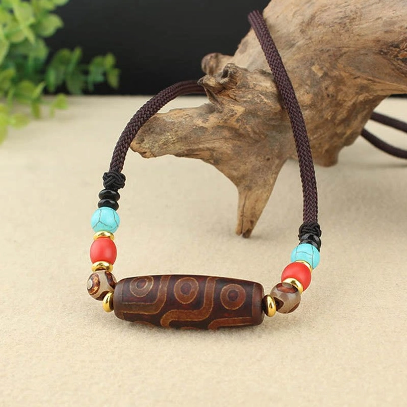 Dzi bead necklace side angled view showing intricate eye patterns and circular markings with turquoise and metal bead accents on wooden surface