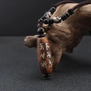 Om Mani Padme Hum Dzi bead pendant necklace side view propped on natural wood display, showing aged agate texture and black beaded chain on dark studio backdrop