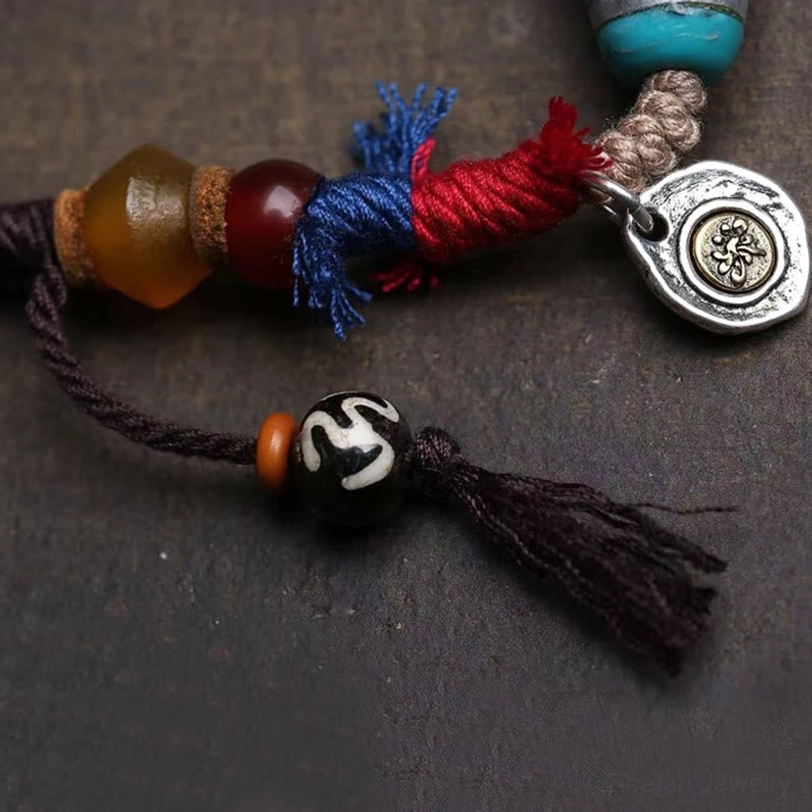 Side profile of handcrafted dzi bead necklace showing cotton cord, agate beads and vintage silver pendant charm