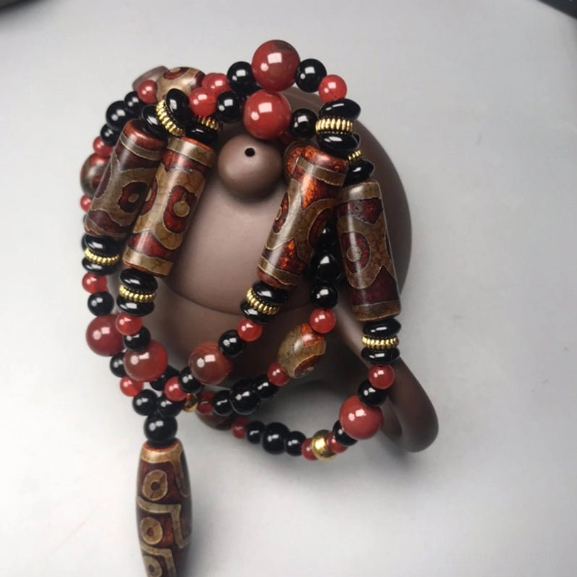 Stacked Dzi bead Tibetan necklaces with patterned beads in close-up, displayed on dark ceramic teapot base