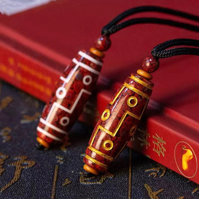 Two styles of cinnabar dzi bead necklaces displayed on vintage book and fabric, gold-patterned and white-patterned variations with black cords