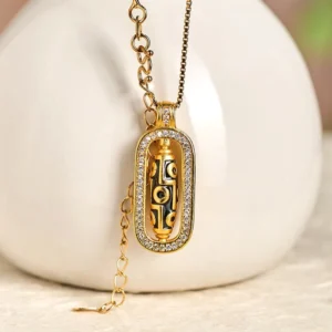 Rotatable Tibetan nine-eye dzi bead necklace with gold chain displayed beside white ceramic vase, three-quarter view