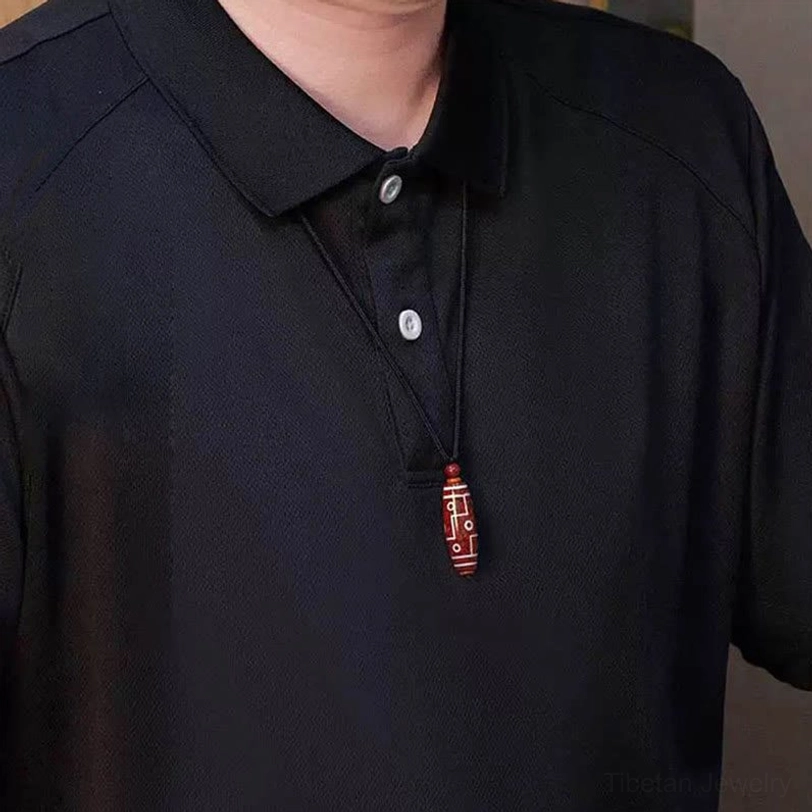 Tibetan dzi bead necklace worn on chest with small red pendant on black cord over casual black shirt, everyday wear styling