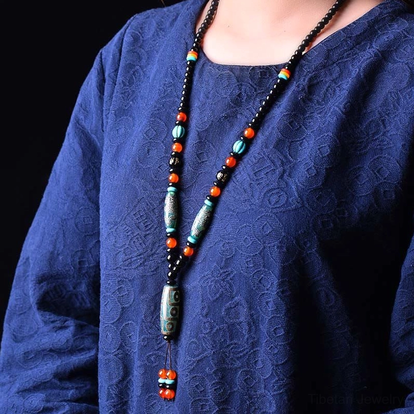 Woman wearing Tibetan Nine-Eye Dzi Bead Dragon Necklace on chest in blue textured clothing