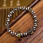 Nine-Eye Dzi Bead Om Mani Padme Hum bracelet with copper accents on wooden surface, oblique angle view showing detailed hand-painted beads and brass spacers