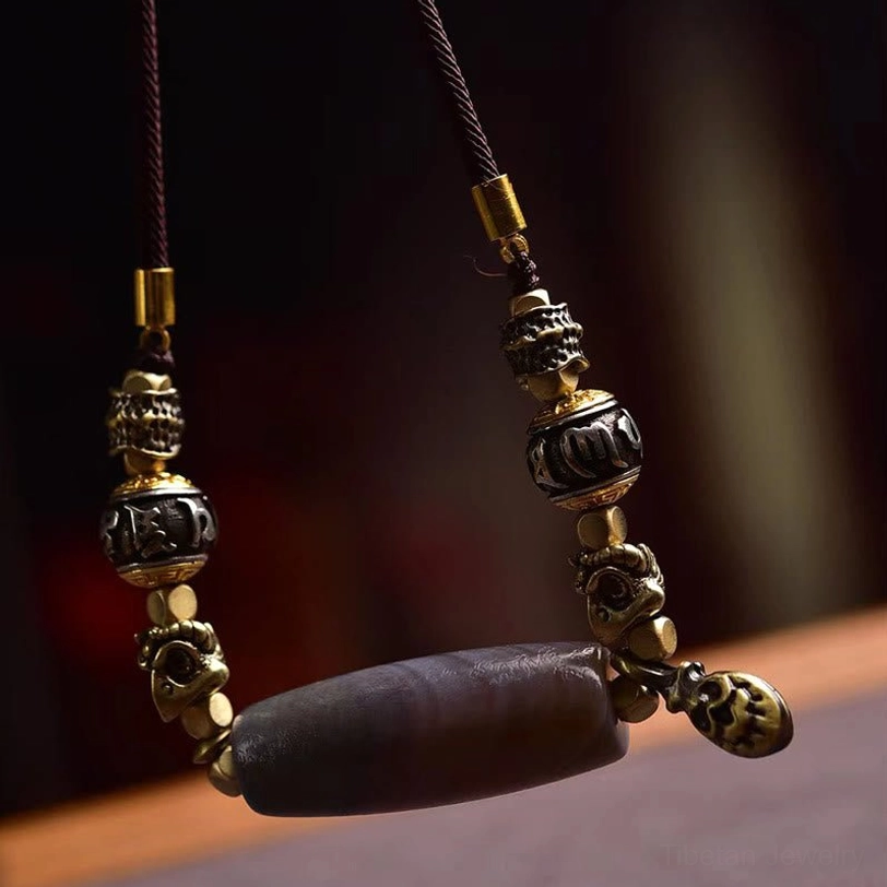 Close-up side view of hand-painted dzi bead pendant with prayer wheel charm and brown wax cord