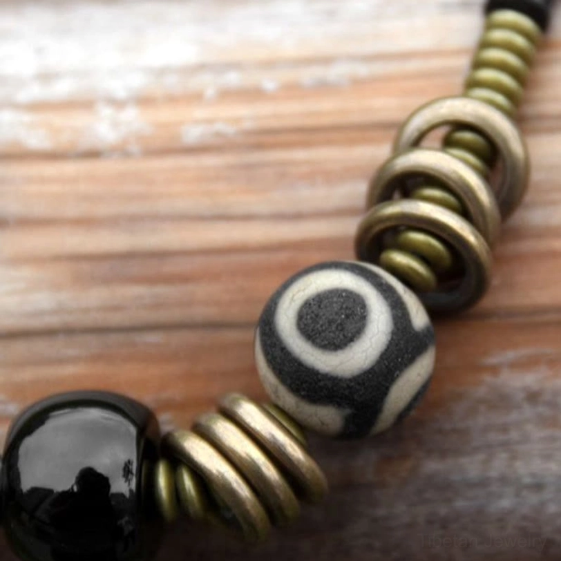 Close-up detail of Tibetan Dzi bead black onyx and brass ring accents on wooden surface