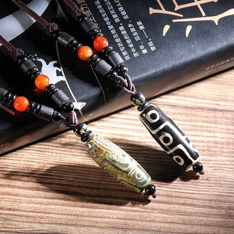 Close-up side view of black and green nine-eye dzi bead pendants with red agate spacer beads