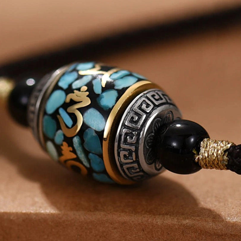 Close-up macro detail of Dzi bead pendant showing turquoise stone inlay, gold Sanskrit script, and silver geometric trim patterns