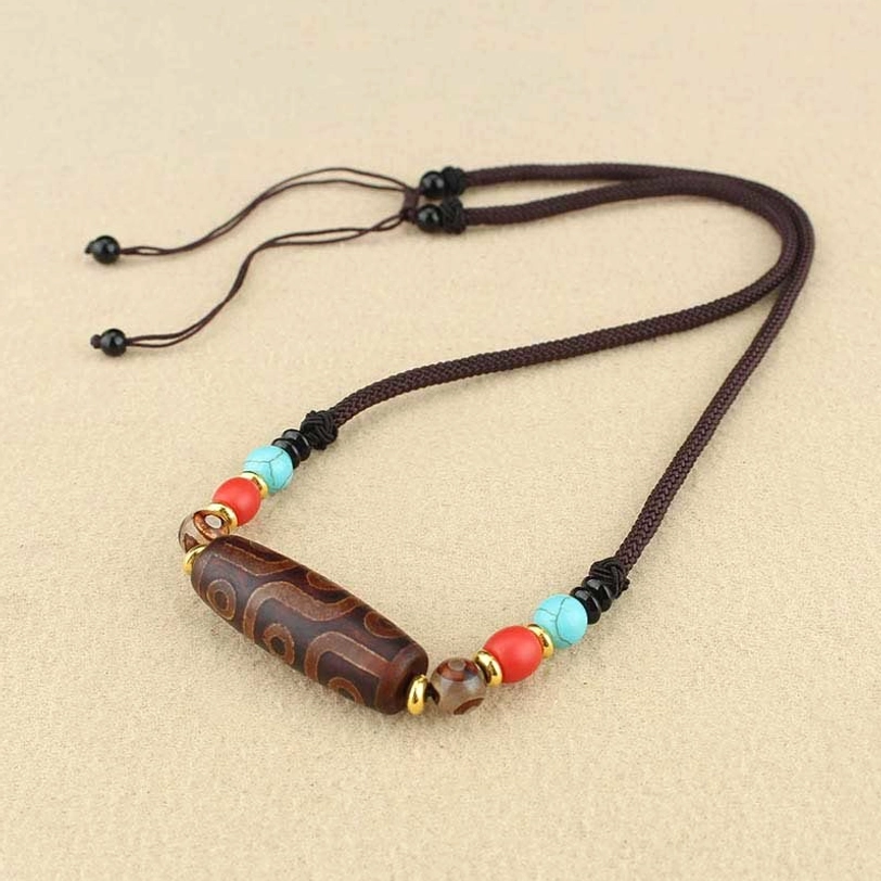 Single dzi bead pendant necklace overhead flat lay with adjustable brown braided cord and colorful gemstone beads on light background