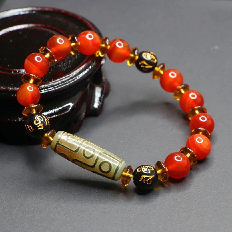 Sacred nine-eye dzi prayer bracelet side view on dark ceramic holder, featuring glossy polished red agate beads and engraved black mantra spacers