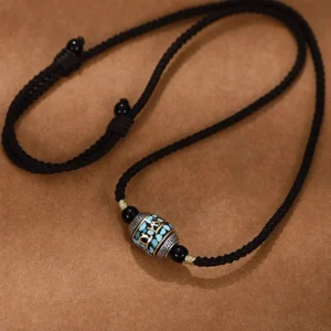 Adjustable Tibetan Dzi bead pendant necklace flat lay showing braided rope chain with metal stopper knots and hand-painted sacred bead