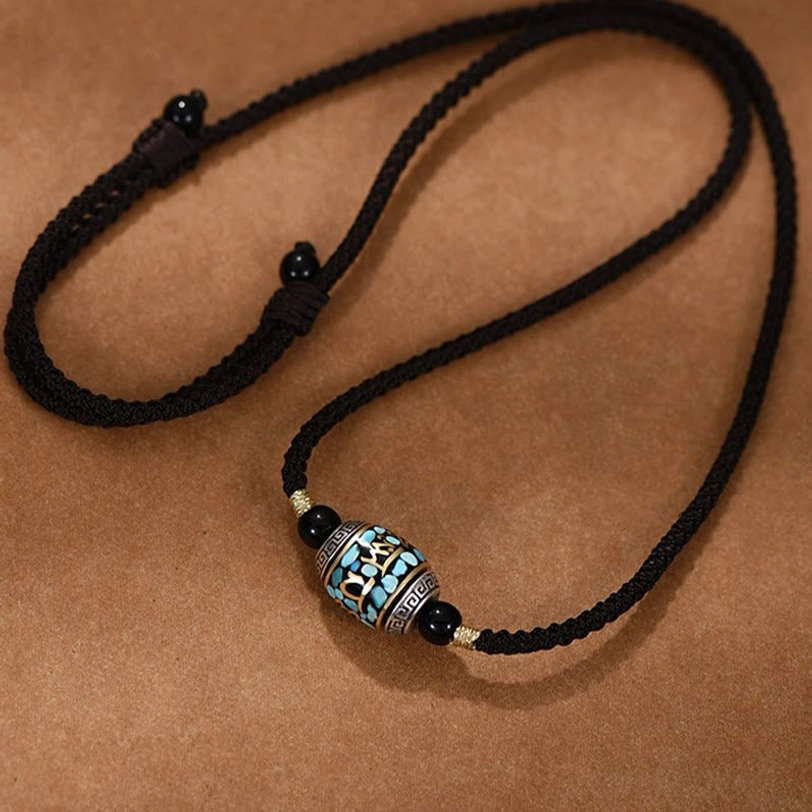Adjustable Tibetan Dzi bead pendant necklace flat lay showing braided rope chain with metal stopper knots and hand-painted sacred bead