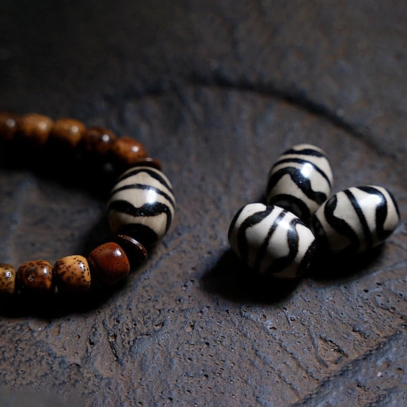 Black and white striped dzi beads displayed with aged bodhi seed bracelet section on dark textured stone surface