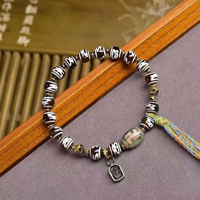 Tibetan Dzi bead bracelet with braided multicolor tassel and stamped metal charm on bamboo background
