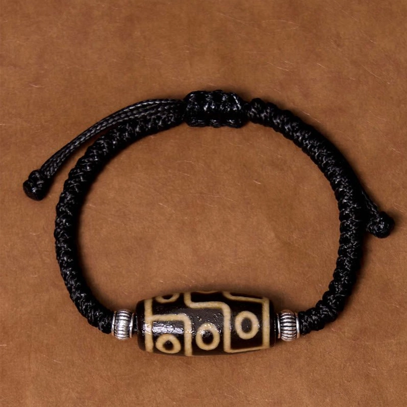 Tibetan dzi bead bracelet flat overhead view showing complete loop with centered nine-eye bead and silver spacers on cardboard