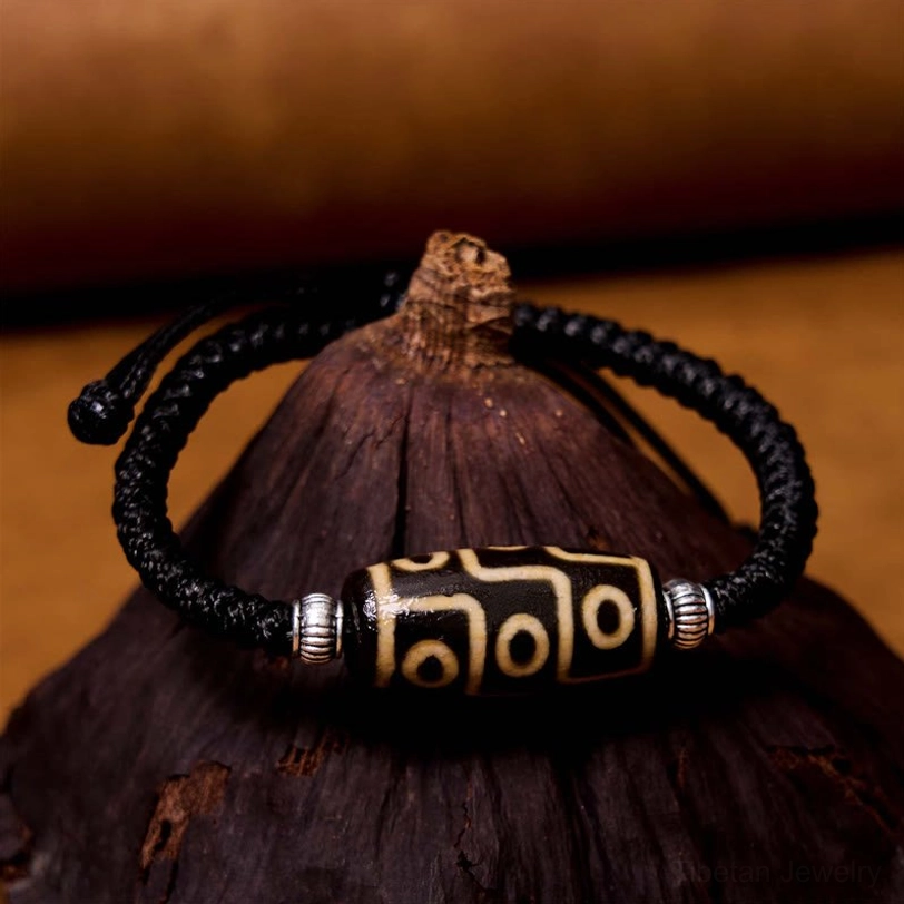 Tibetan dzi bead bracelet top-down front view on dark wooden prop displaying silver spacers and nine-eye design