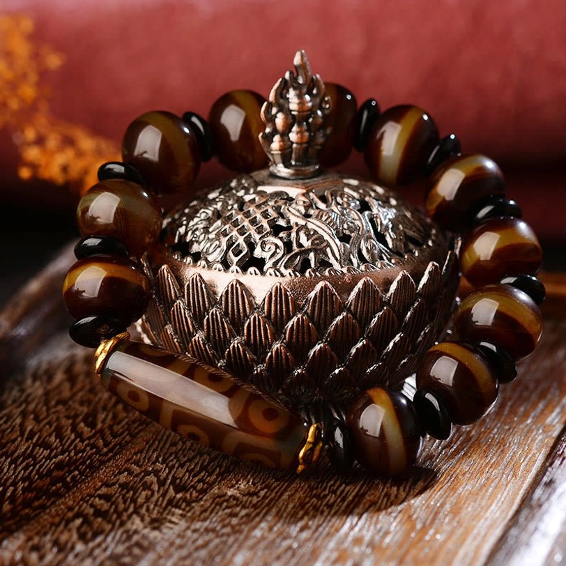 Dzi agate bracelet styled with ornate silver incense burner on wooden table with red fabric, showcasing Tibetan spiritual aesthetic