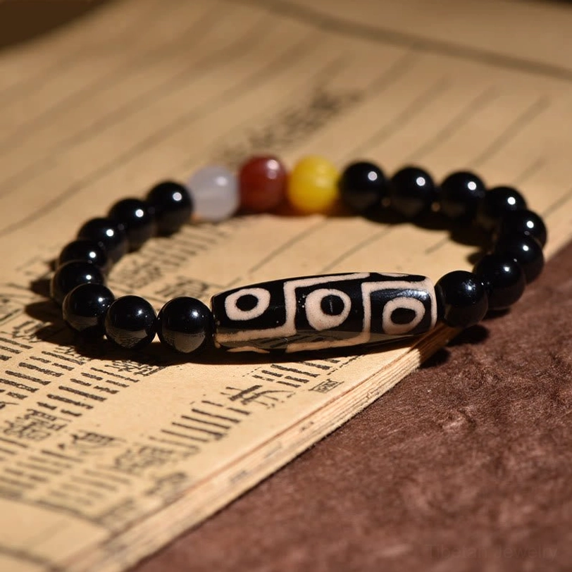 Side overhead view of nine-eye dzi bead bracelet on antique scroll background, with dzi bead positioned horizontally flanked by black round beads and warm-toned spacers