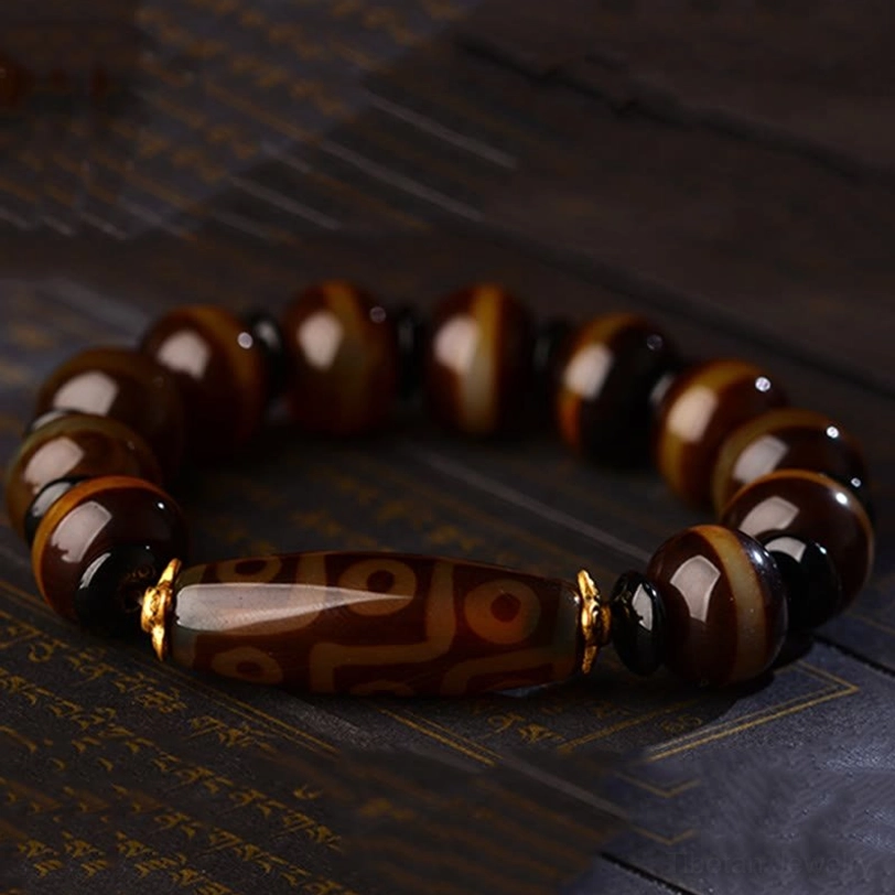 Dzi agate bracelet with uniform striped agate beads and central nine-eye dzi bead on vintage printed paper background with gold spacers