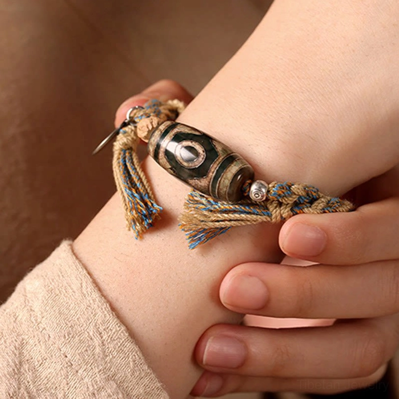 Nine-eye dzi bead bracelet worn on wrist close-up fit braided rope silver tag