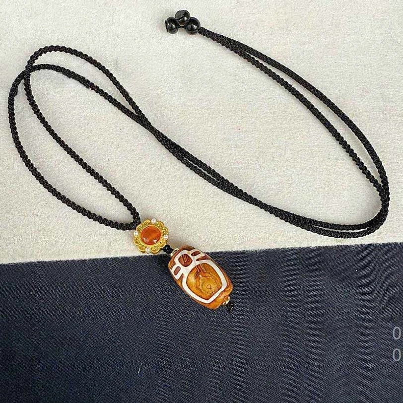 Full length side view of nine-eye dzi bead necklace showing complete braided cord and pendant