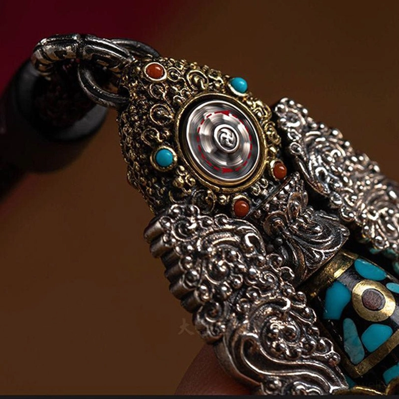 Rotatable center detail of dzi pendant in side close-up, displaying spinning metal wheel center with turquoise and red gem accents and carved silver details