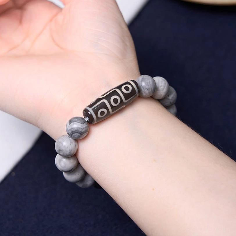Tibetan dzi bead bracelet on wrist against dark fabric, displaying authentic nine-eye dzi stone and grey picasso jasper beads