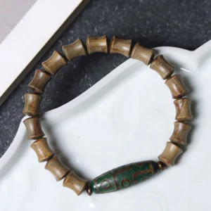 Nine-eye dzi green sandalwood bracelet oblique angle display on white ceramic surface showing curved bracelet arrangement