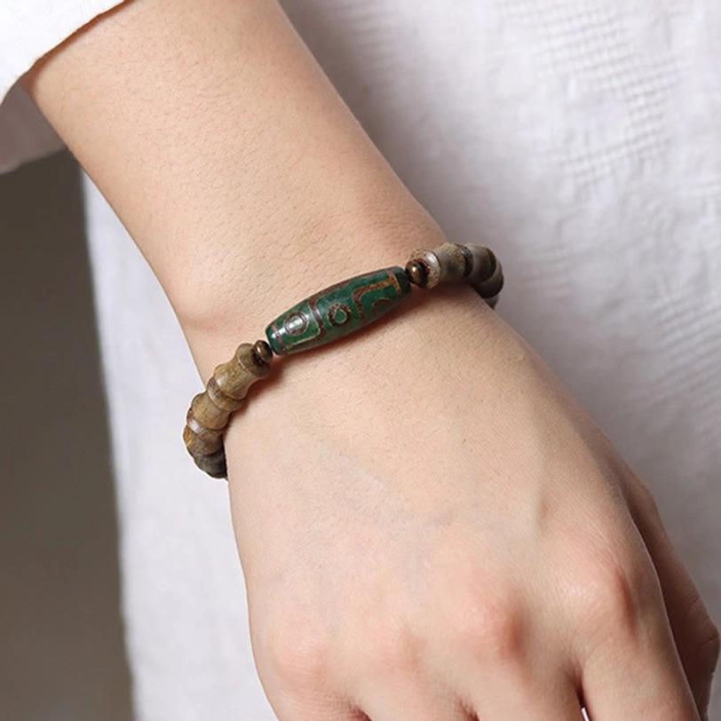 Tibetan nine-eye dzi green sandalwood bracelet close-up wrist view worn on human wrist plain fabric background