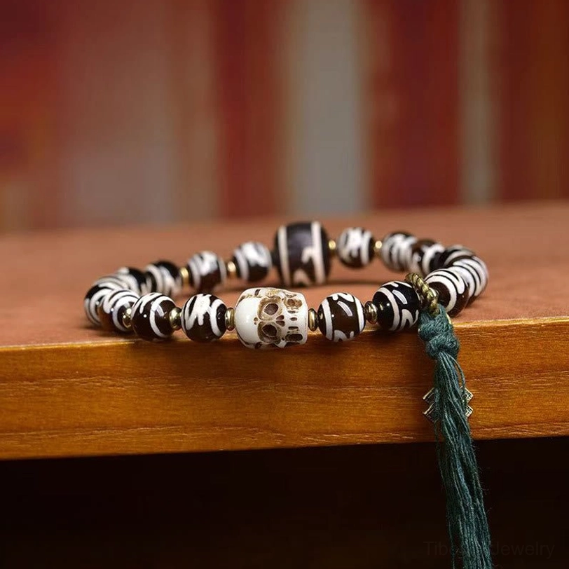 Sacred Tibetan Dzi bead skull bracelet flat lay on wood surface with curved positioning and long green tassel