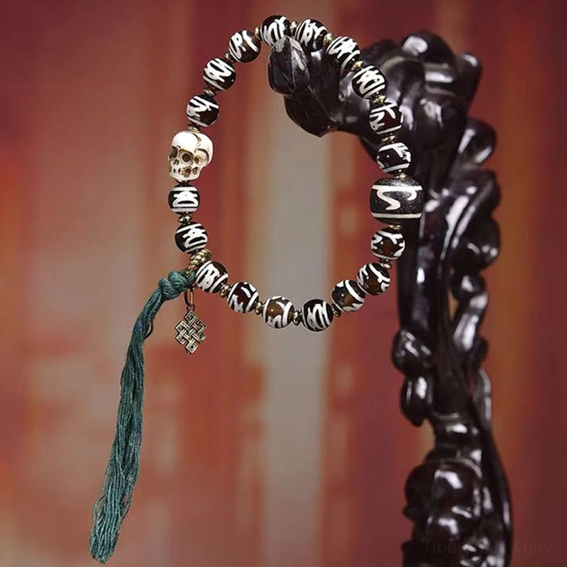 Tibetan skull bead bracelet displayed on black wooden stand showing full length with green tassel accent
