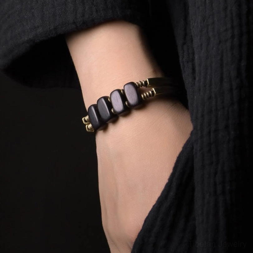 Tibetan ebony beaded bracelet worn on wrist, side close-up shot displaying rectangular dark ebony beads with brass spacer beads in minimal style against black textured background