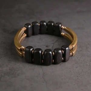 Circular tibetan ebony and brass beaded bracelet, direct top view on dark grey background, featuring oval dark ebony beads with brass hardware spacers in closed loop configuration