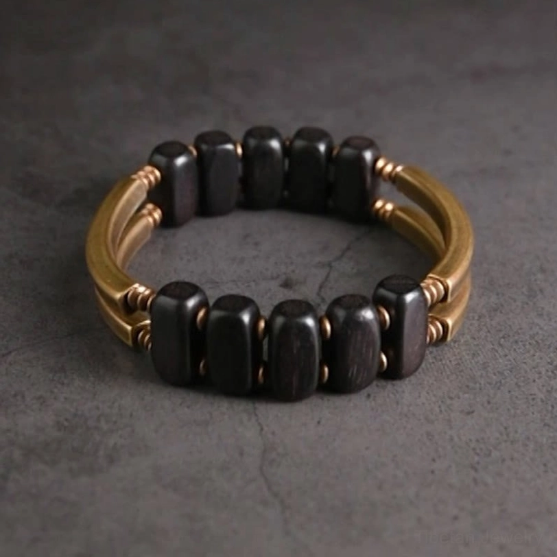 Circular tibetan ebony and brass beaded bracelet, direct top view on dark grey background, featuring oval dark ebony beads with brass hardware spacers in closed loop configuration