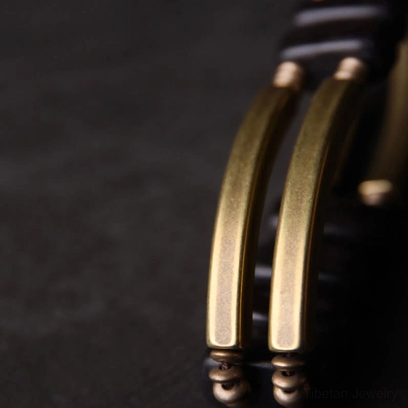 Macro close-up of ebony brass bracelet joints and hardware, side macro view on dark grey background showing brushed gold brass bars with screw-style spacers and smooth metal texture