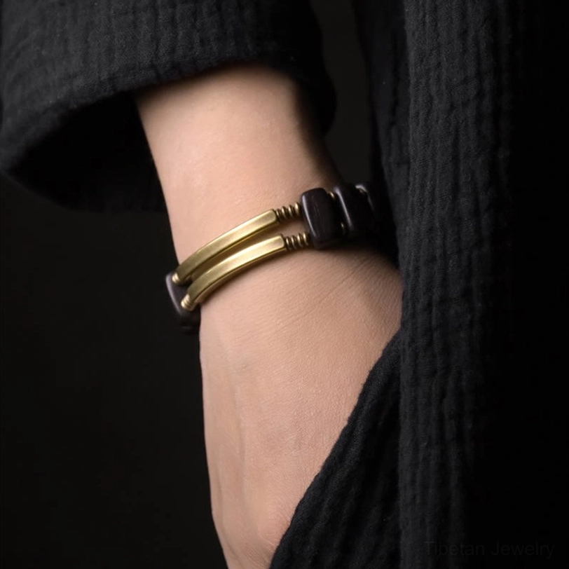 Tibetan ebony wood brass bracelet worn on wrist side close-up, showing black ebony beads with brushed gold metal accents fitted on skin against textured black clothing