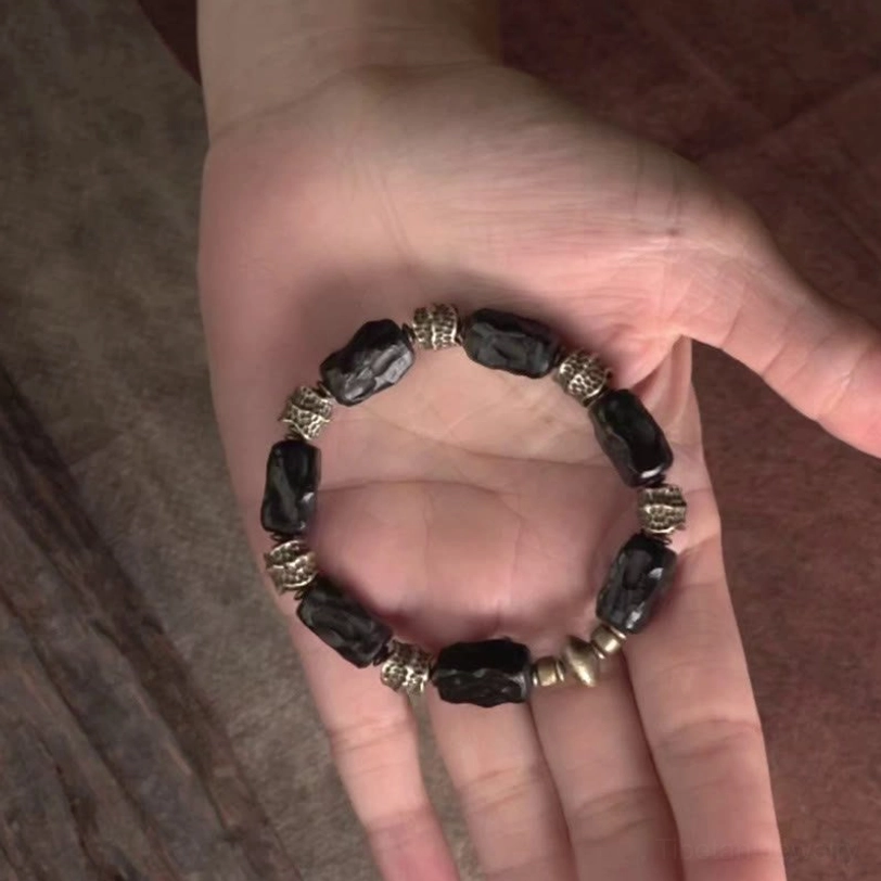 Ebony copper beaded bracelet resting on open palm showing full bead layout with dark wood beads and bronze metal accents