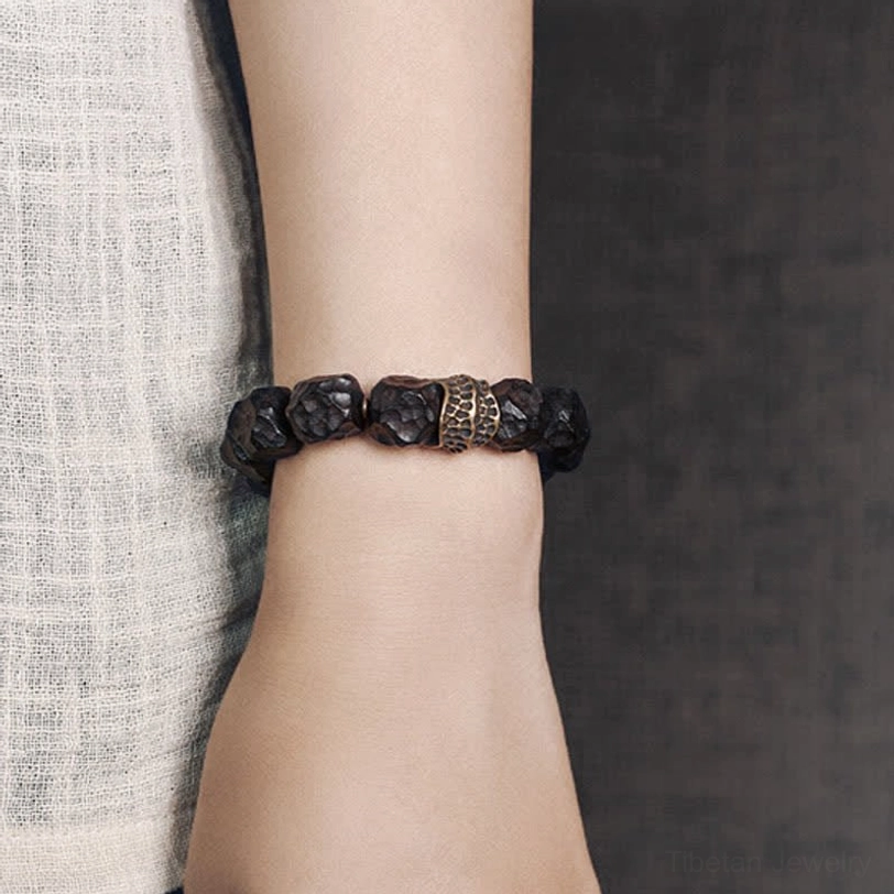 Side profile of ebony and copper couple bracelet with bronze textured spacer bead on dark fabric background
