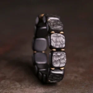 Close-up side three-quarter view of handcrafted ebony wood bracelet showing hammered texture and gold metal fasteners