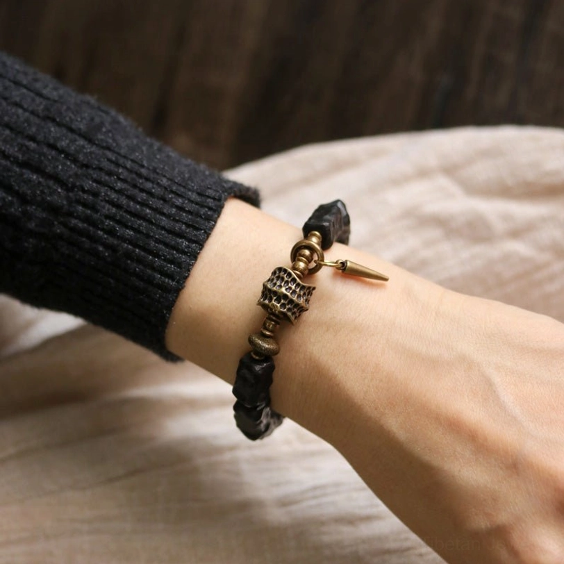 Close-up wrist view of ebony wood copper bracelet showing spike charm and textured wooden beads