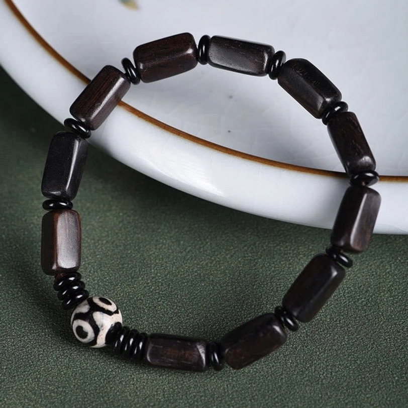 Overhead view of ebony wood and Dzi bead Tibetan protection bracelet on white ceramic surface