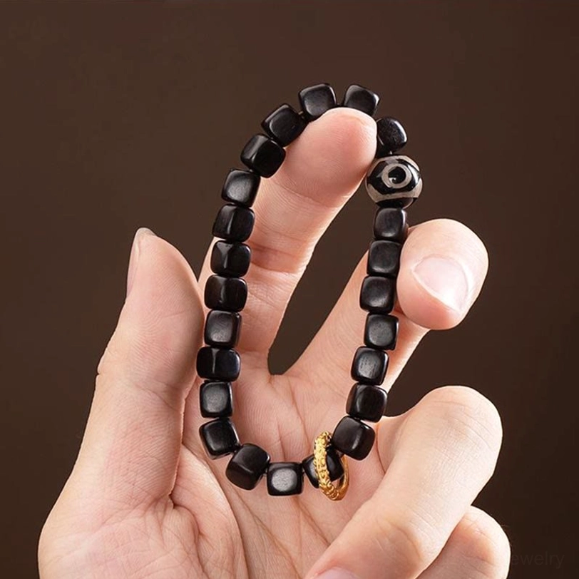 Ebony wood dzi bead bracelet held in hand close-up showing detailed beadwork and metal ring