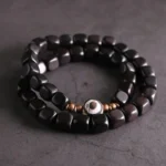 Ebony wood nine-eye dzi bead couple bracelet with copper accents, top-down flat lay view on dark cracked stone